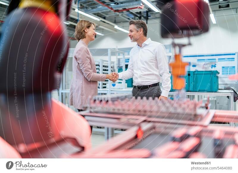 Businessman and businesswoman shaking hands in a modern factory hall business life business world business person businesspeople associate associates