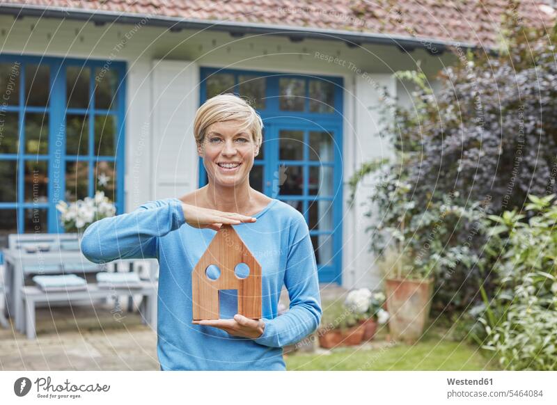 Portrait of smiling woman standing in front of her home holding house model females women models portrait portraits houses smile Adults grown-ups grownups adult
