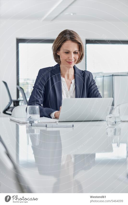 Businesswoman using laptop at desk in office desks Laptop Computers laptops notebook offices office room office rooms businesswoman businesswomen business woman