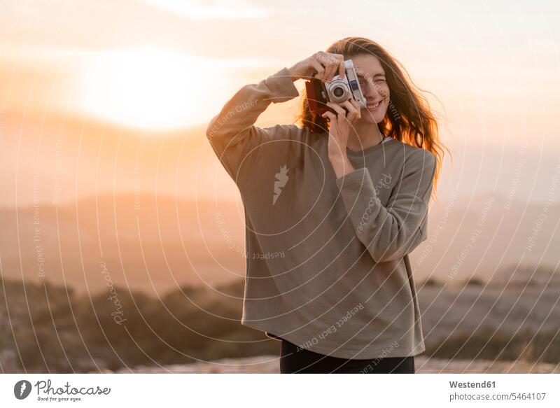 Spain, Barcelona, Natural Park of Sant Llorenc, woman taking a picture with vintage camera at sunset females women sunsets sundown photographing cameras Adults