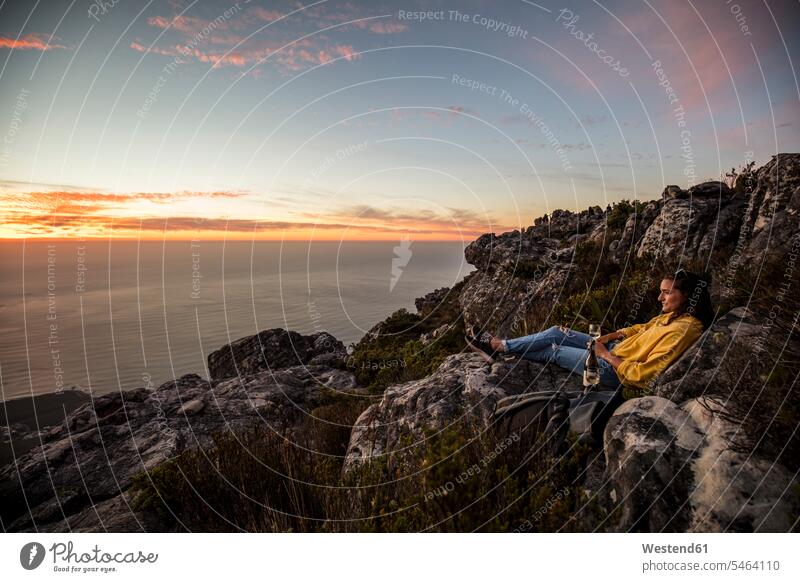 South Africa, Cape Town, Table Mountain, woman sitting on a rock drinking wine at sunset rocks females women sunsets sundown Seated Wine Adults grown-ups