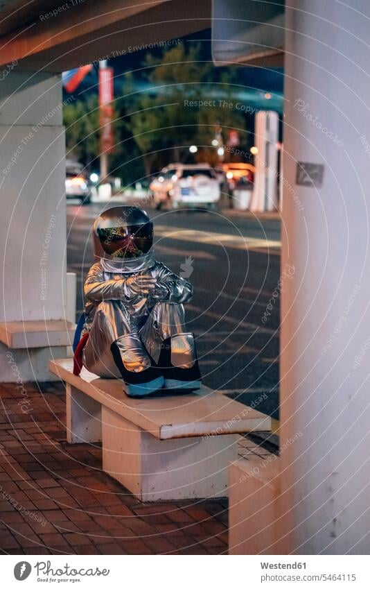 Spaceman sitting on bench at a bus stop at night astronaut astronauts busstops spaceman spacemen by night nite night photography Seated benches astronautics