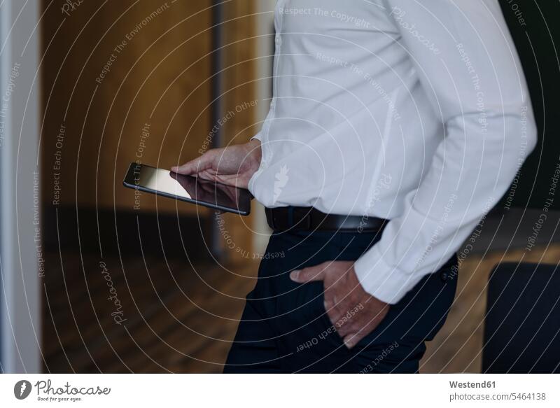 Businessman with hands in pockets holding digital tablet while standing at office color image colour image indoors indoor shot indoor shots interior