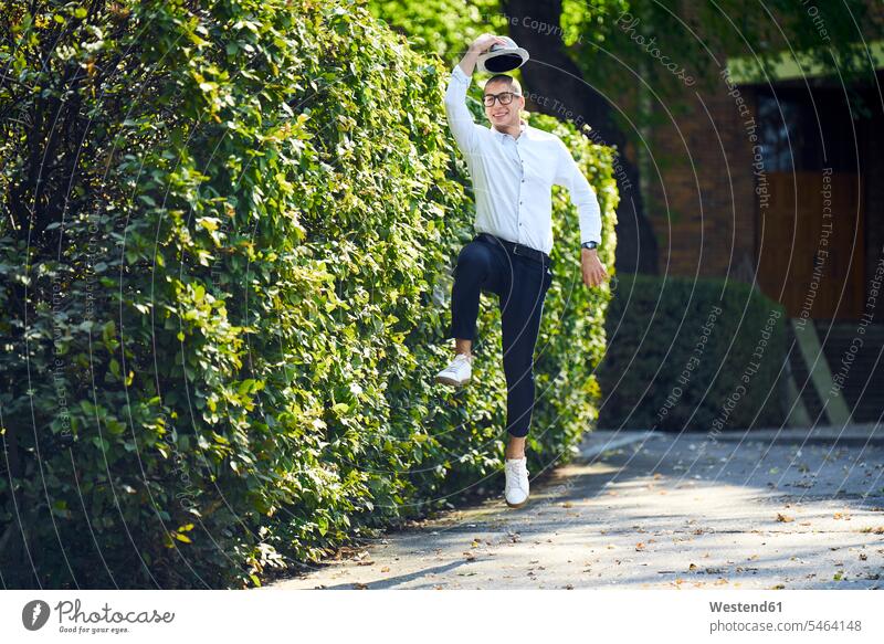 Happy young man jumping around at a hedge Mixed Race Person mixed-race Person mixed race ethnicity unconventional Offbeat lifestyle life styles mischief