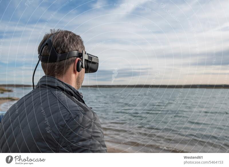 Man wearing VR glasses at lakeshore specs Eye Glasses spectacles Eyeglasses Lakeshore Lake Shore lakeside man men males virtual reality water waters