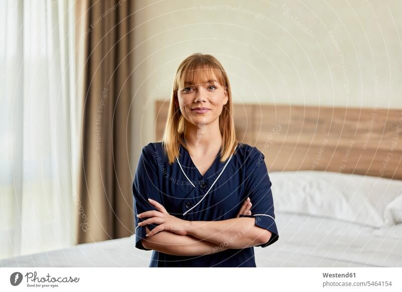 Confident chambermaid with arms crossed standing in bedroom at hotel color image colour image indoors indoor shot indoor shots interior interior view Interiors
