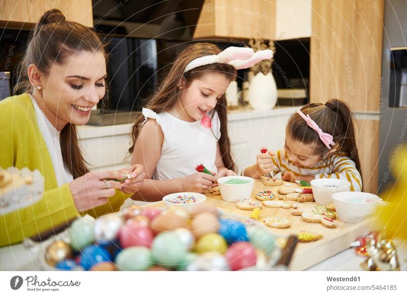 Mother with daughters decorating Easter cookies in kitchen mother mommy mothers ma mummy mama decorate Biscuit Cookie Cooky Cookies Biscuits girl females girls