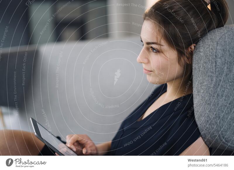 Young businesswoman sitting on couch with digital tablet looking at distance human human being human beings humans person persons caucasian appearance