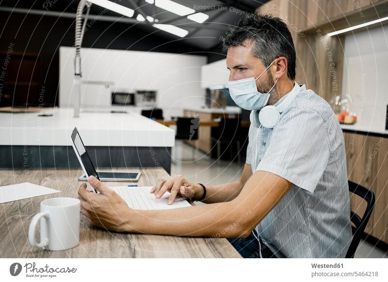 Businessman wearing protective mask while using laptop at desk in office during COVID-19 pandemic color image colour image Spain indoors indoor shot