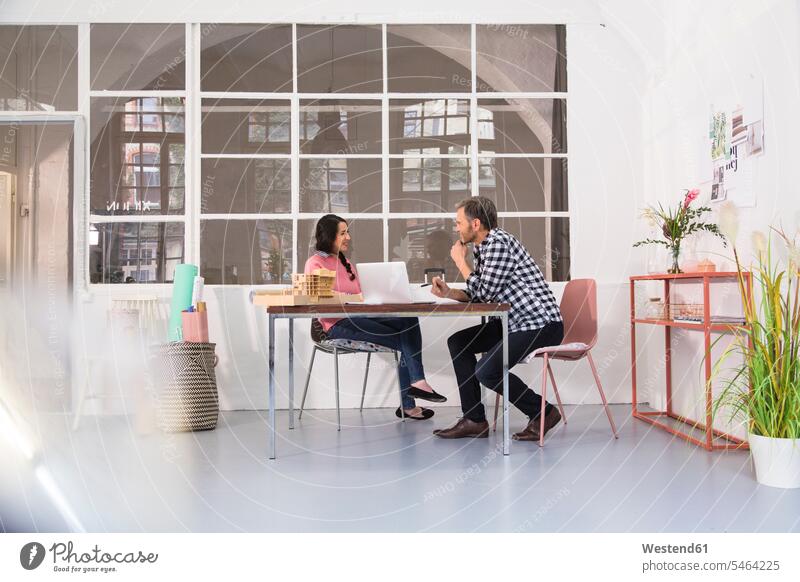 Smiling colleagues sitting at table in an architect's loft office architect's office lofts offices office room office rooms smiling smile Seated Table Tables