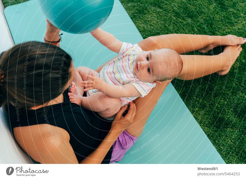 Young mother and baby exercising on yoga mat, playing with a ball balls exercise practising train training Seated sit happy closeness propinquity