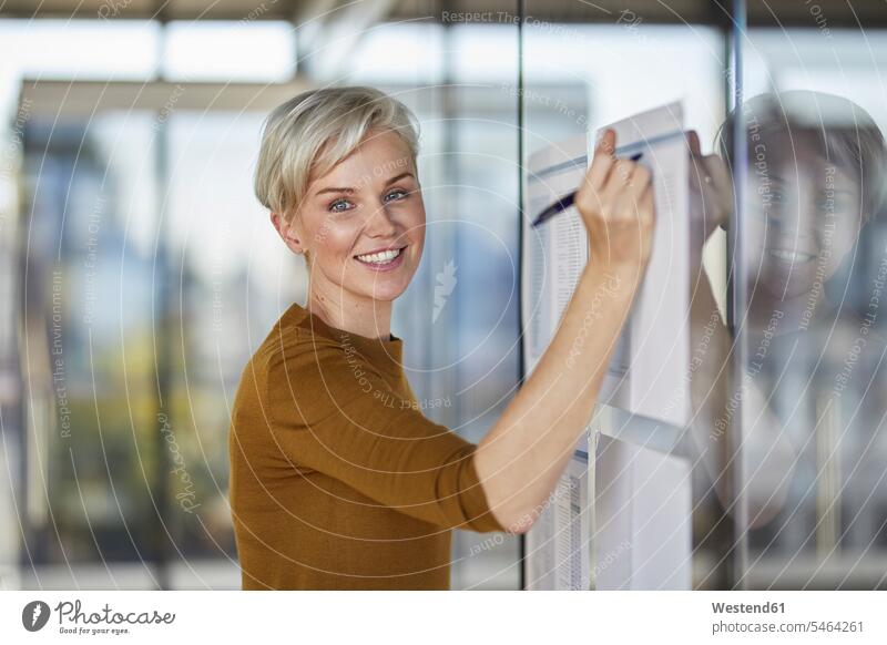 Portrait of smiling businesswoman writing on papers at glass pane write smile portrait portraits glass panes confidence confident businesswomen business woman