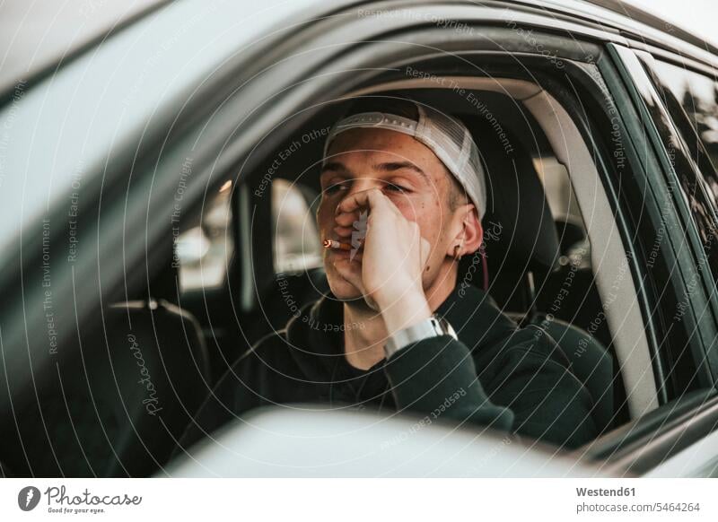 Young man smoking cigarette while driving car outdoors location shots outdoor shot outdoor shots day daylight shot daylight shots day shots daytime color image