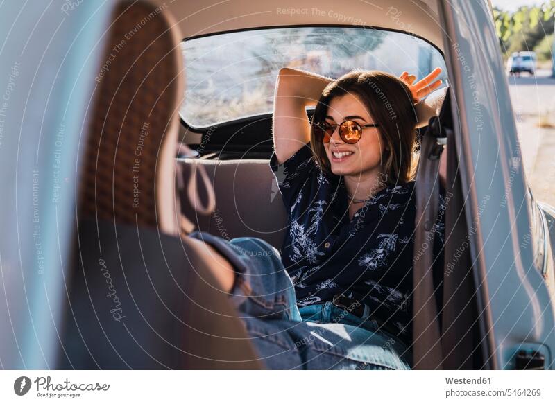 Smiling young woman wearing sunglasses sitting in a car females women smiling smile automobile Auto cars motorcars Automobiles sun glasses Pair Of Sunglasses
