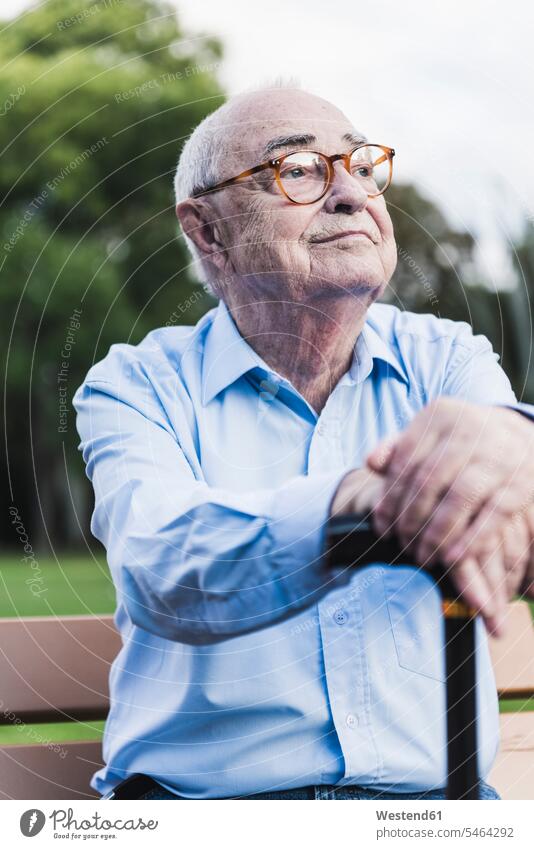 Portrait of senior man in a park leaning on his walking stick shirts benches park benches Eye Glasses Eyeglasses specs spectacles Seated sit relax relaxing