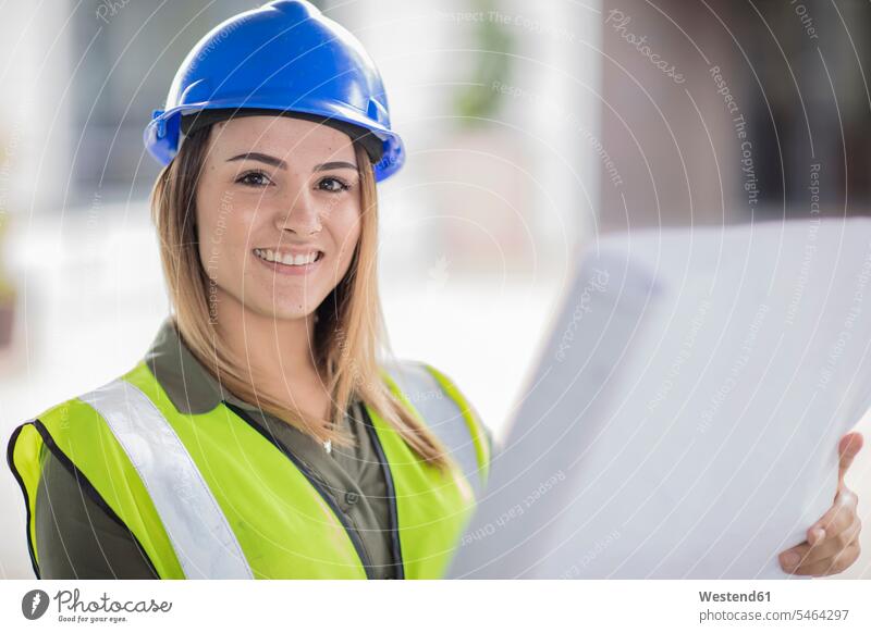 Portrait of smiling woman wearing hard hat and reflective jacket holding plan reflective vest reflector-vest reflector vest reflective vests hard hats hardhats