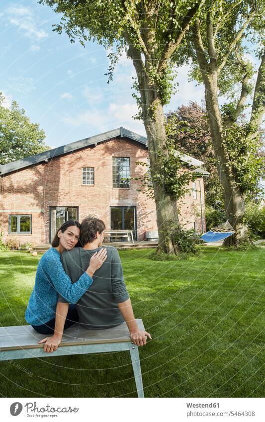 Affectionate couple sitting in garden of their home twosomes partnership couples house houses gardens domestic garden Seated people persons human being humans