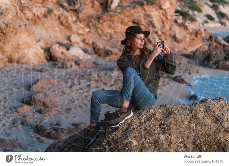 Young woman using smartphone on beach during sunset, Ibiza images picture pictures photo photographs photos hats smile Seated sit in the evening Late Evening