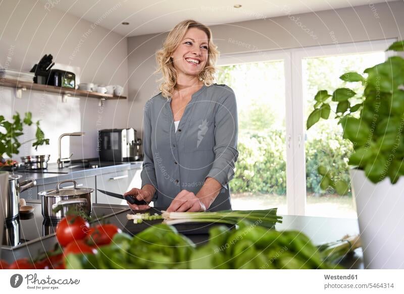 Smiling woman cutting spring onions in kitchen domestic kitchen kitchens green onion females women smiling smile Vegetable Vegetables Food foods food and drink