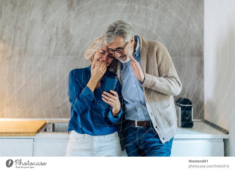 Mature couple using cell phone together in kitchen at home telecommunication phones telephone telephones cell phones Cellphone mobile mobile phones mobiles