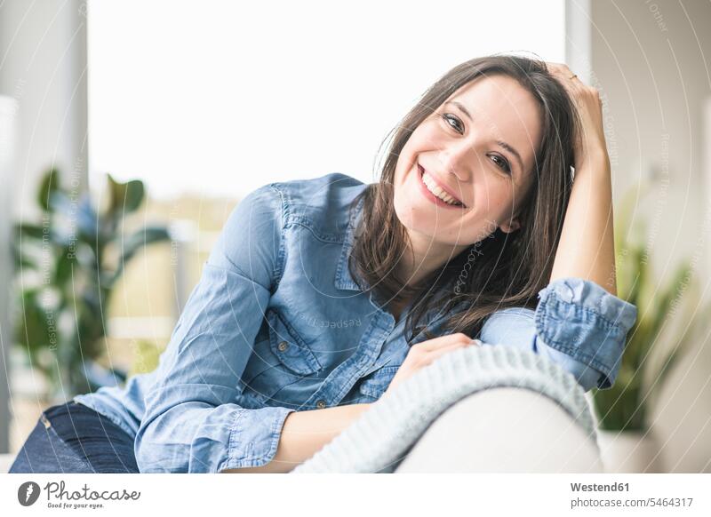 Portrait of happy woman sitting on the couch at home Seated females women happiness portrait portraits settee sofa sofas couches settees Adults grown-ups