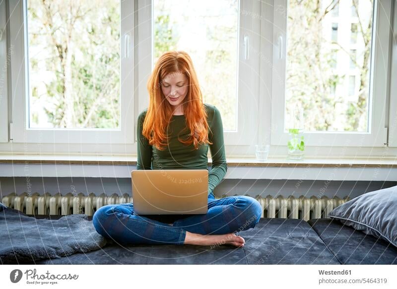 Redheaded woman sitting in front of window using laptop females women Seated use windows Laptop Computers laptops notebook Adults grown-ups grownups adult