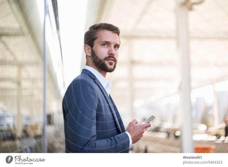 Young businessman holding cell phone looking sideways Businessman Business man Businessmen Business men looking away look away mobile phone mobiles