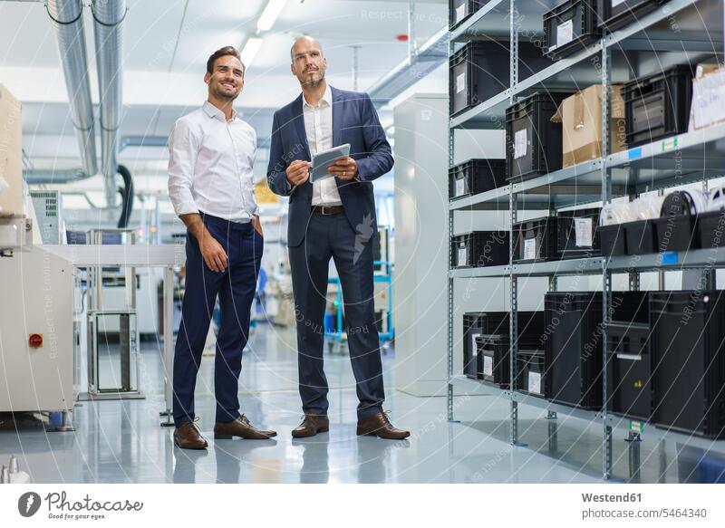Businessman holding digital tablet while standing by smiling engineer and looking away at factory color image colour image indoors indoor shot indoor shots