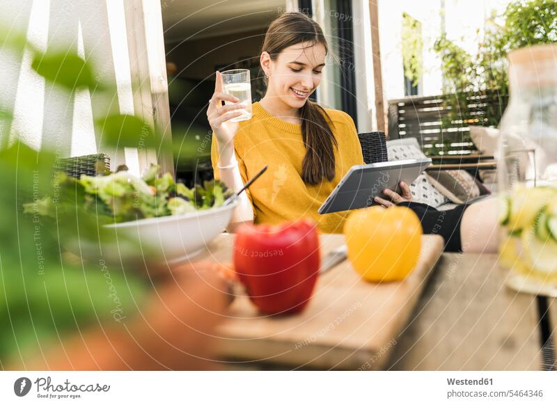 Smiling young woman with vegetables on table watching video over digital tablet at home color image colour image Germany casual clothing casual wear