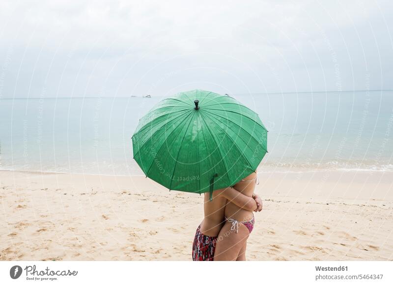 Thailand, boy hugging his mother on the beach under a green umbrella mommy mothers ma mummy mama boys males embracing embrace Embracement beaches umbrellas