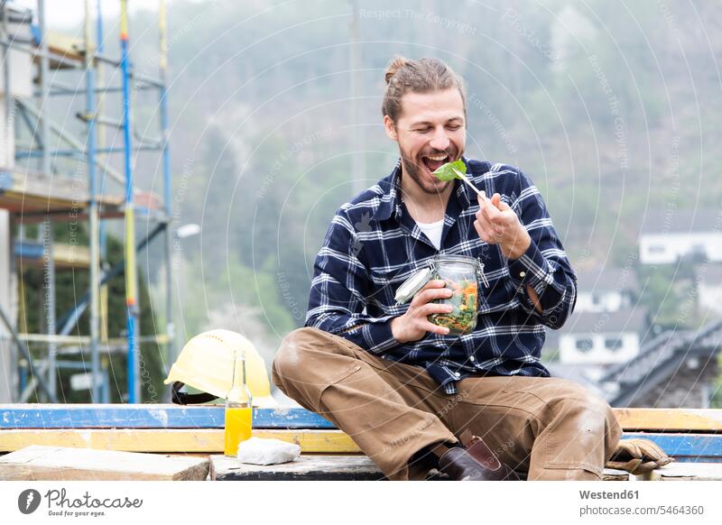 Construction worker eating salad while sitting outdoors at construction site color image colour image Germany Architecture Building Site Building Sites