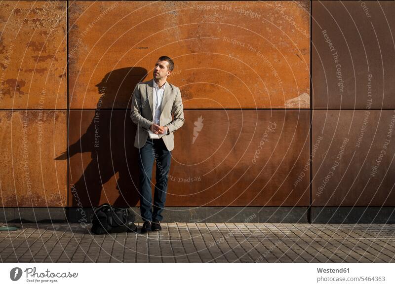 Businessman standing at a wall holding a notebook walls Business man Businessmen Business men notebooks business people businesspeople business world