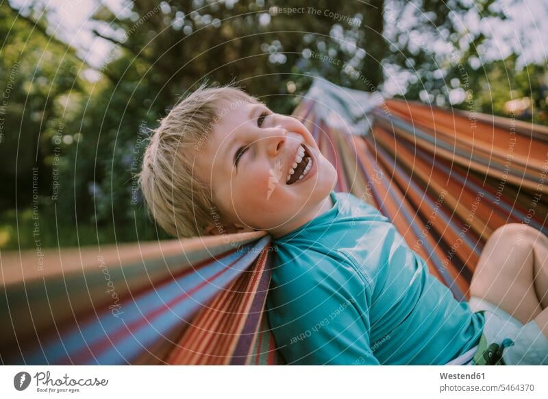 Cheerful boy relaxing on hammock at garden during sunny day color image colour image Germany outdoors location shots outdoor shot outdoor shots daylight shot