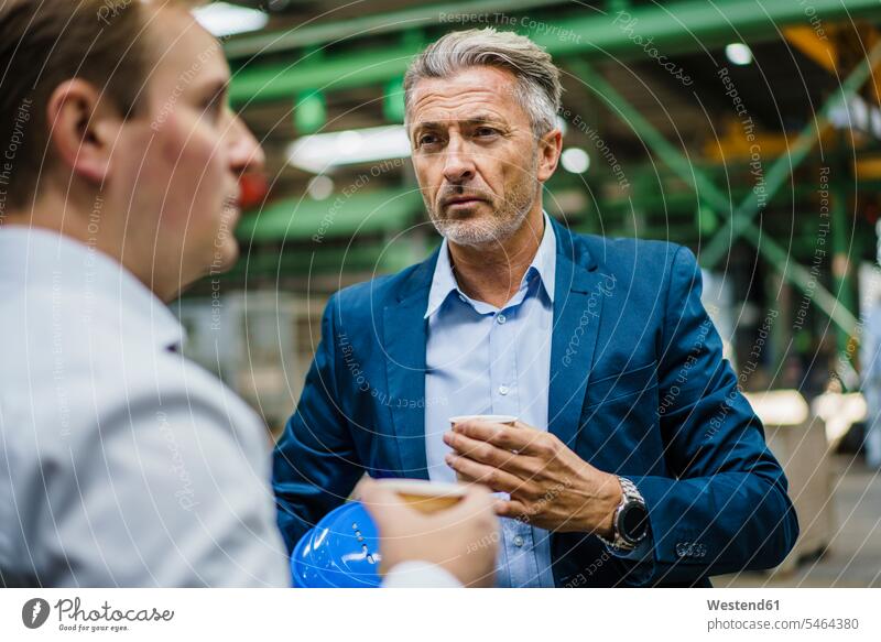 Two businessmen with coffee having a meeting in a factory colleague Occupation Work job jobs profession professional occupation superior supervisor the boss
