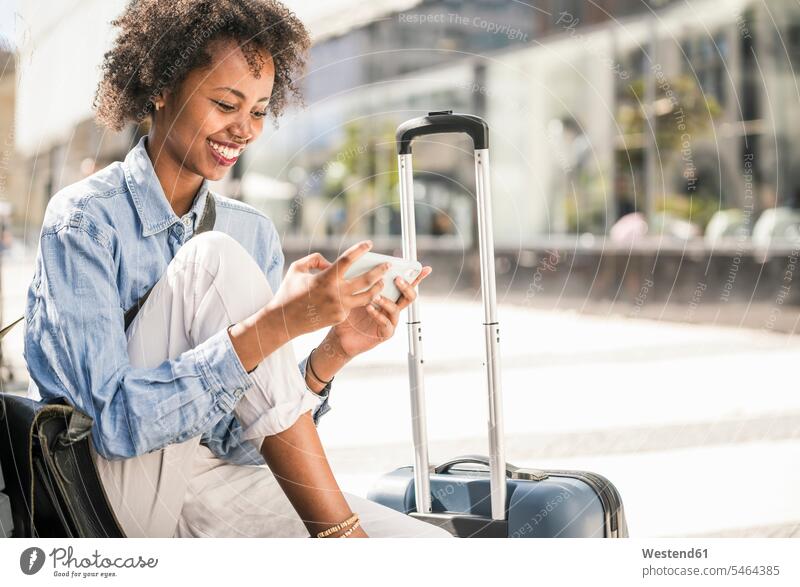 Happy young woman sitting on a bench with suitcase using cell phone human human being human beings humans person persons 1 one person only only one person adult