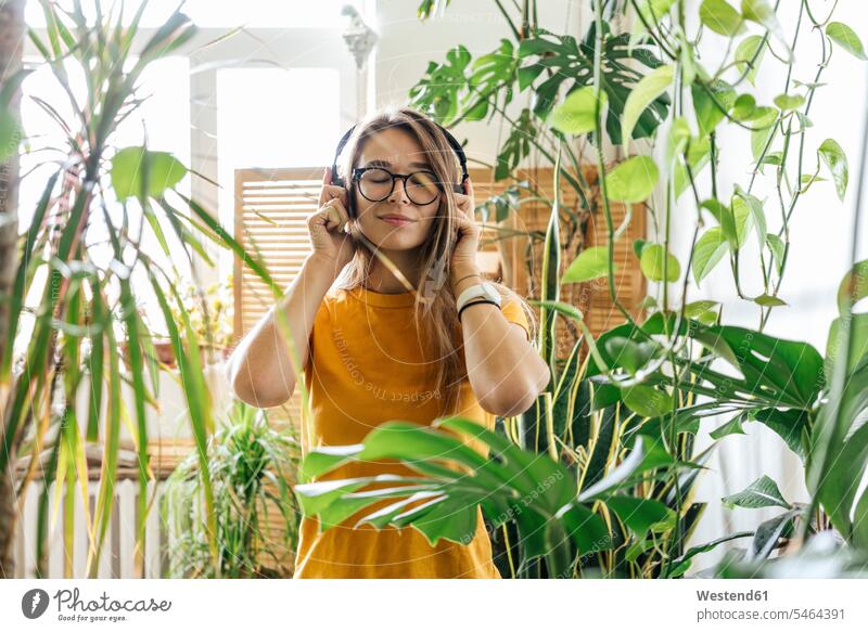 Young woman surrounded by plants listening to music with headphones windows T- Shirt t-shirts tee-shirt headset Eye Glasses Eyeglasses specs spectacles hear