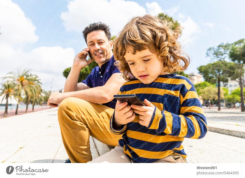 Spain, Barcelona, father and son both with a smartphone sons manchild manchildren fathers daddy dads papa Smartphone iPhone Smartphones family families people