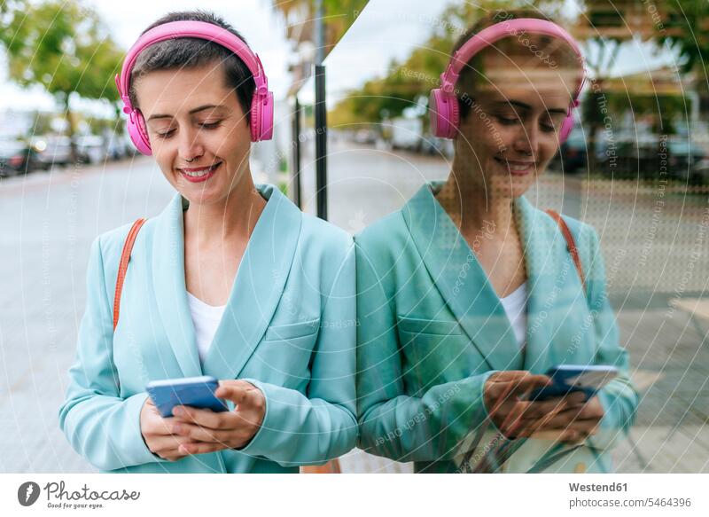 Woman dressed in jacket listening to music with her mobile phone suit coat suit jacket woman females women Smartphone iPhone Smartphones hearing headphones