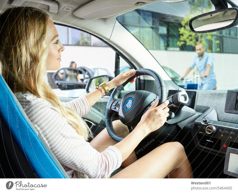 Smiling woman driving electric car drive females women smiling smile automobile Auto cars motorcars Automobiles Adults grown-ups grownups adult people persons