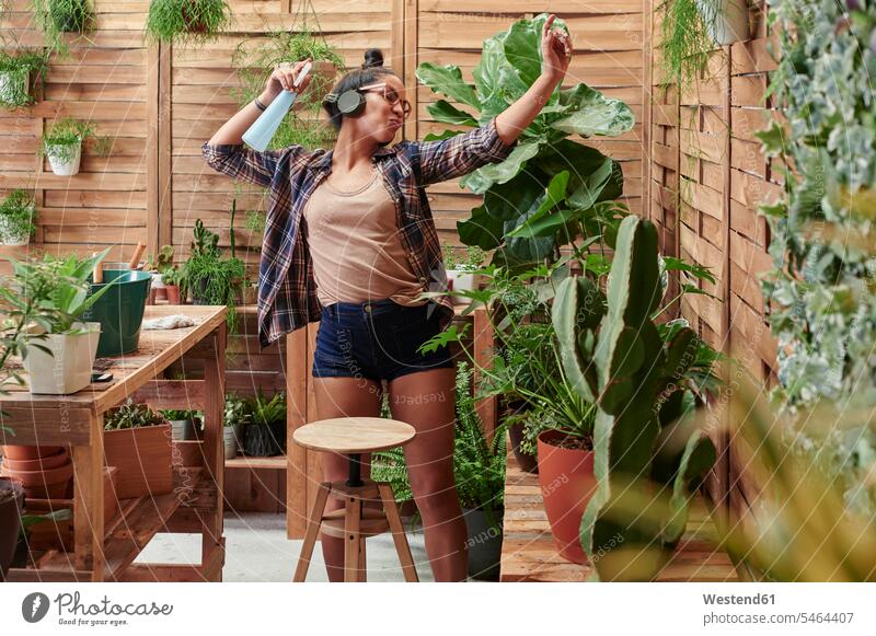 Happy young woman dancing on her terrace while gardening gardeners flower pot flower pots flowerpots Tables wood wood table headphone headset Eye Glasses