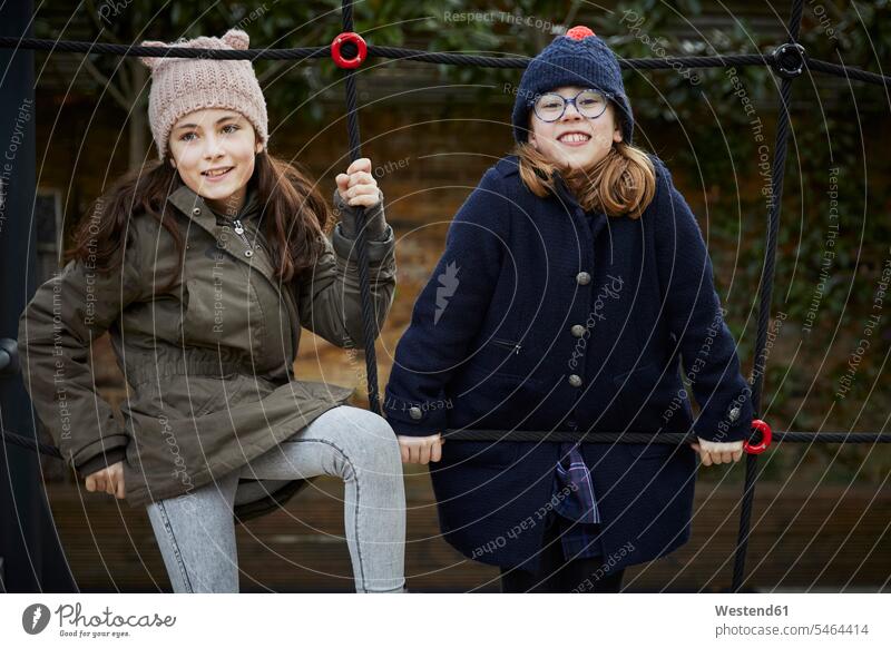 Two girls on the schoolyard playground during break time friends mate female friend pupils schoolchild schoolchildren coat coats jackets relax relaxing smile