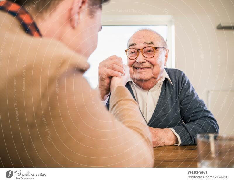 Smiling senior man arm wrestling with young man senior men elder man elder men senior citizen males senior adults Adults grown-ups grownups people persons