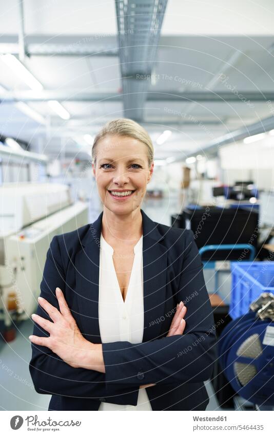 Smiling mature blond female professional standing with arms crossed at illuminated industry color image colour image indoors indoor shot indoor shots interior