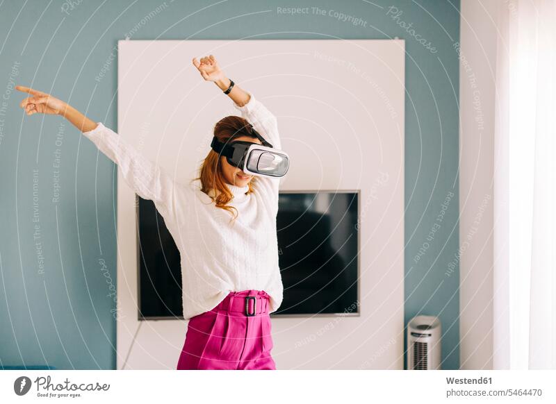 Happy young woman wearing VR glasses at home human human being human beings humans person persons celibate celibates singles solitary people solitary person