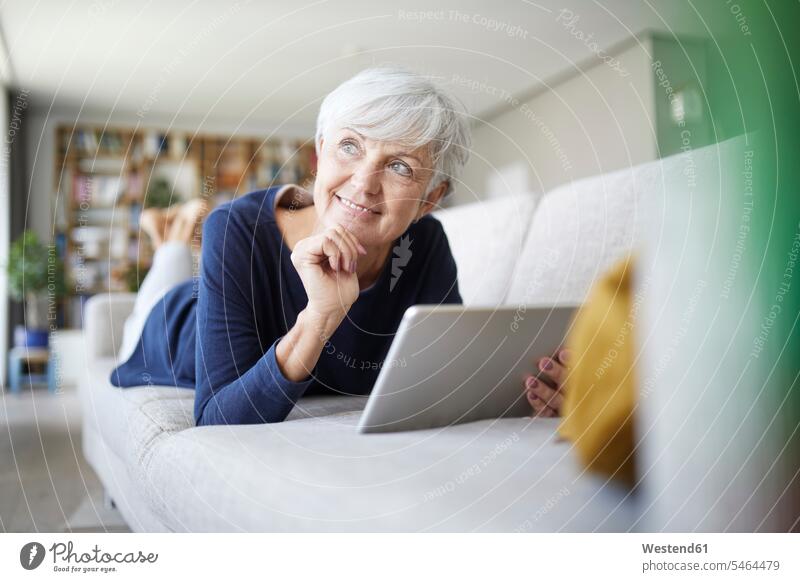 Senior woman with hand on chin using digital tablet while lying on sofa at home color image colour image indoors indoor shot indoor shots interior interior view