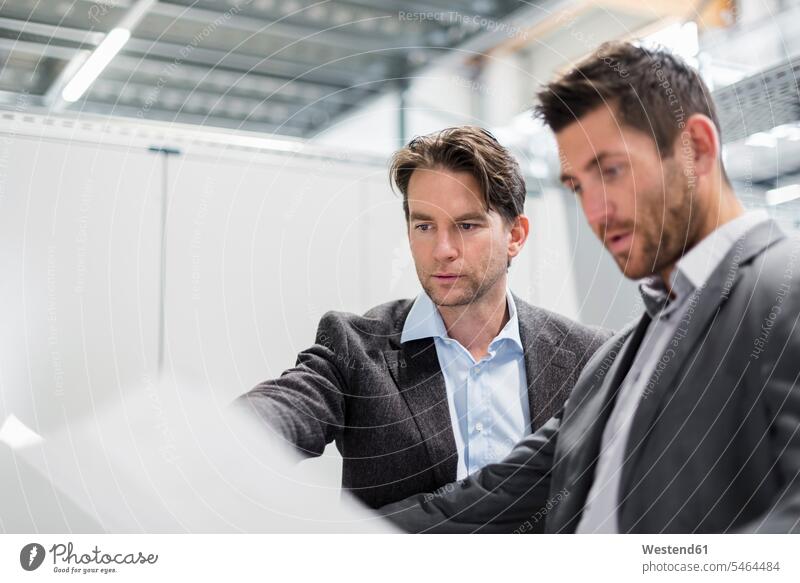 Two businessmen looking at plan in modern factory factories Businessman Business man Businessmen Business men plans contemporary eyeing business people