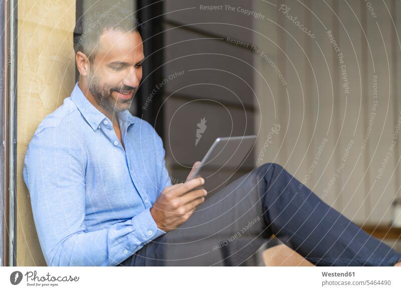 Smiling businessman sitting at the window using tablet Germany reflection reflexion Reflecting reflections reflexions wireless Wireless Connection