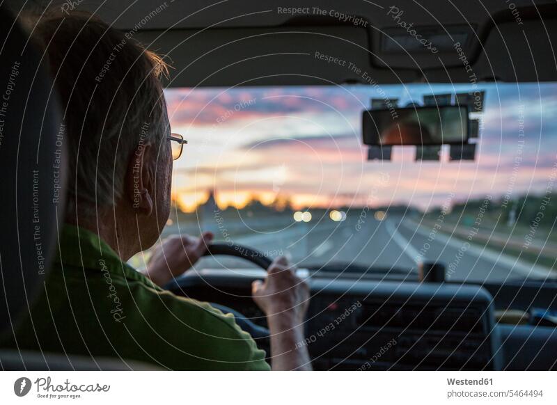 Senior man driving a car on a highway at sunset transport motor vehicles road vehicle road vehicles Auto automobile Automobiles cars motorcar motorcars