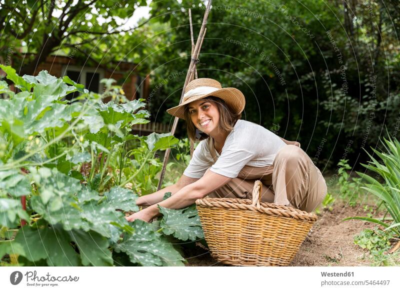 Smiling young woman wearing hat working in vegetable garden during curfew color image colour image Spain dungarees Bib Overalls Bibs Overall Bibs Overalls