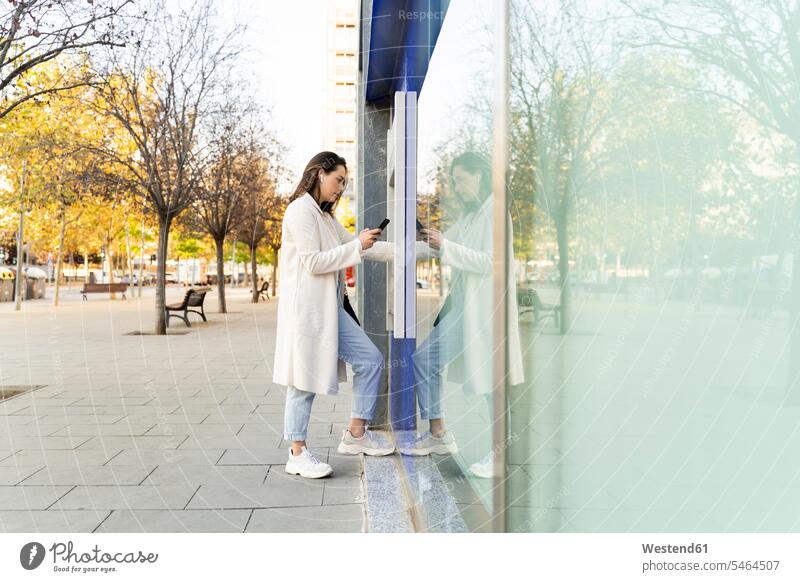 Businesswoman withdrawing money from ATM while standing on footpath in city color image colour image outdoors location shots outdoor shot outdoor shots day